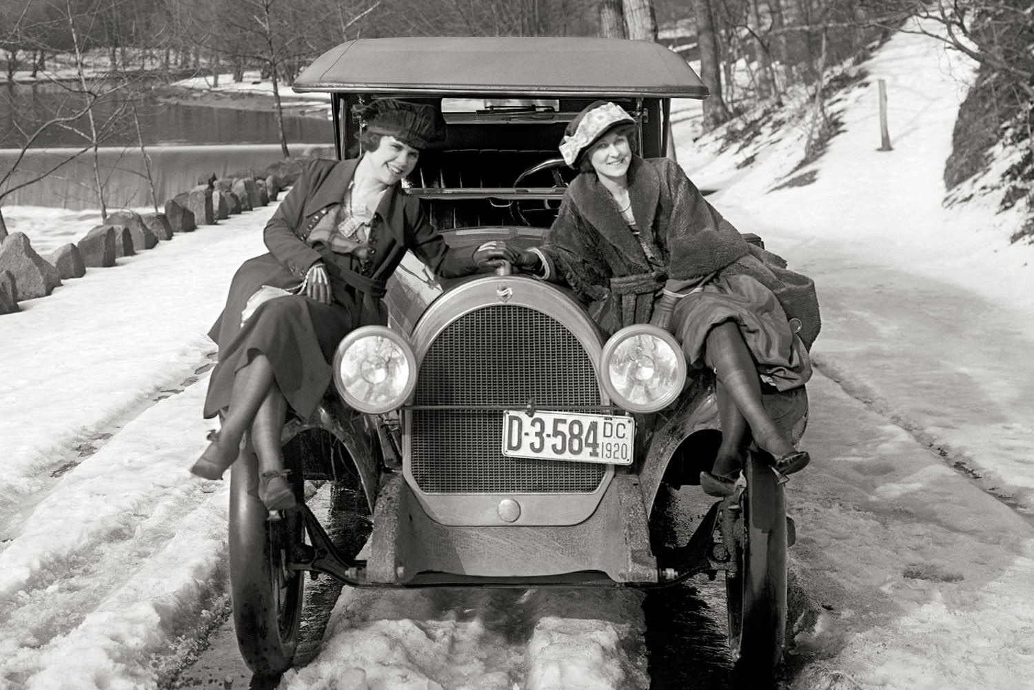 two girls posing with an old car